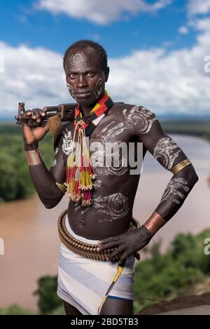 Mit seinem Gewehr und seiner Körperfarbe hoch über dem Omo River, einem Karo-Stamm oder ethnischen Gruppenmitglied, Tumi, Äthiopien. Stockfoto