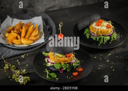 Leckere gegrillte Veggie Burger mit Kichererbsen und Gemüse auf schwarzem Brot auf dunkler Holzplatte. Stockfoto