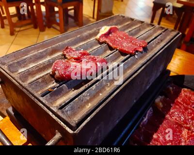 Große Scheiben Rote-Ox-Fleisch mit Fett bestreut mit grobem Salz auf einem Grill, der zum Kochen auf einem Grill angezündet wird Stockfoto
