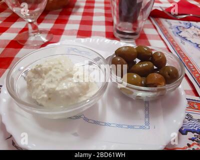 Zwei transparente Schüsseln mit mediterranen Alioli-Sauce und schwarzen Oliven auf einem rot-weiß kariertem Tischtuch Stockfoto