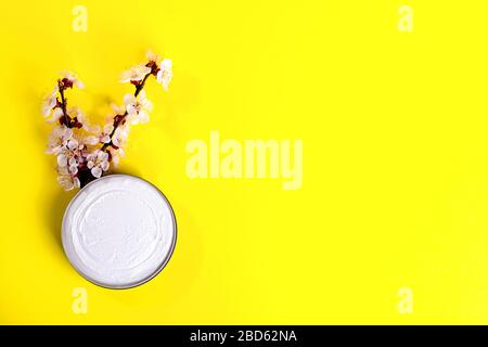 Kosmetische Creme im Mixbecher und Perücke von blühendem Baum mit rosafarbenen Blumen auf hellgelbem Hintergrund. Hautpflegekonzept mit natürlichen Cremes. Draufsicht. Flach Stockfoto