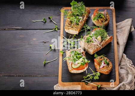 Bruschetten und Kanapees mit putenpate und Mikrogrüns auf einem dunklen rustikalen Hintergrund. Traditionelle mediterrane Küche. Köstliches hausgemachtes Frühstück Stockfoto