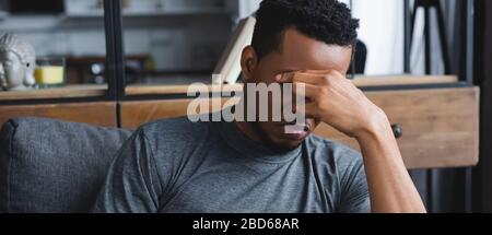 Panoramaaufnahme eines depressiven afroamerikanischen Mannes, der zu Hause auf dem Sofa sitzt Stockfoto
