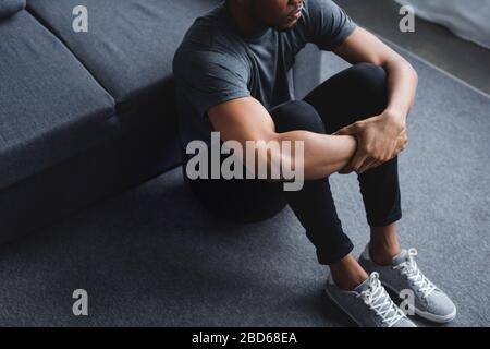 3/4-Blick auf den traurigen afroamerikanischen Mann, der zu Hause auf dem Boden sitzt Stockfoto