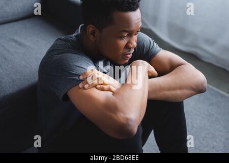 Depressiver afroamerikanischer Mann, der mit gekreuzten Armen auf dem Boden sitzt Stockfoto