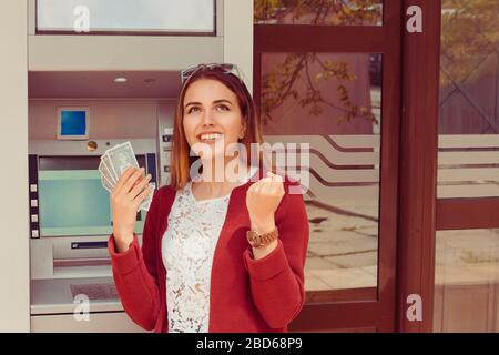 Zurückziehen. GELDAUTOMAT. Portrait fröhliche lächelnde Frau exultiert pumpende Fäuste ecstatic feiert Erfolg beim halten von Bargeld-Banknoten isolierte Outsi Stockfoto