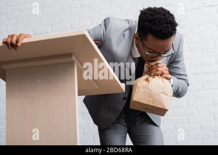 Nervöse afroamerikanische Unternehmer atmen mit Papiertüten und haben Panikattacken während der Geschäftskonferenz im Büro Stockfoto