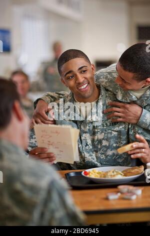 Der junge Soldat blickt über die Schulter seines Freundes, während er einen Brief seines jungen Sohnes liest, während er im Armeesaal Frühstück isst. Stockfoto
