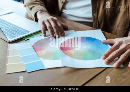 3/4-Ansicht der männlichen Hände mit Papieren in der Nähe des Laptops am Tisch im feigen Raum Stockfoto