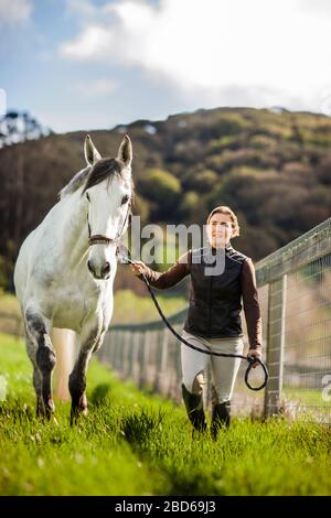 Mitte der erwachsenen Frau, die ihr Pferd in einem Grasigen Weide. Stockfoto