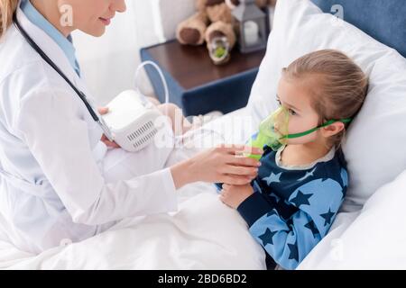 Arzt in weißem Mantel mit Atemschutzmaske bei asthmatischem Kind mit Kompressor-Inhalator Stockfoto