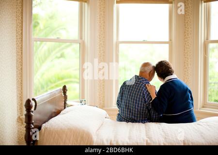 Älteres Paar sitzt auf dem Bett, beide in Morgenmantel. Stockfoto