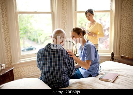 Unwohl älterer Mann, der einen Besuch von seiner Krankenschwester und seiner erwachsenen Tochter erhält. Stockfoto