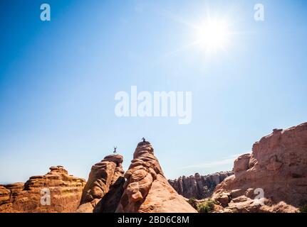 Ein Mann, der vor Freude über eine Sandsteinfhin im Arches National Park springt, während sein Freund sein Bild macht. Utah, USA. Stockfoto