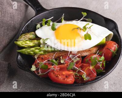 Gebratenes Ei auf Toast mit geröstetem Tomatenspargelfrühstück, gesundes Essen Stockfoto