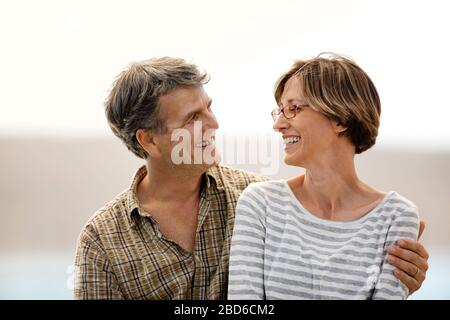 Lächelndes Paar mittleren Alters zusammen an einem Strand sitzen. Stockfoto