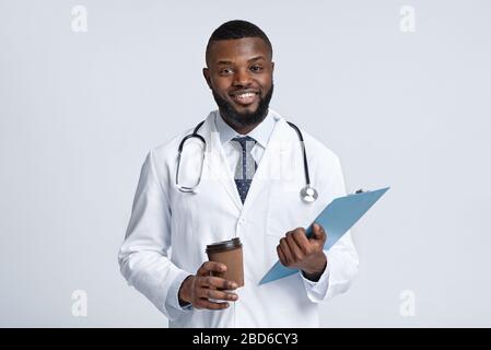 Glücklicher afrikanischer männlicher Therapeut mit medizinischer Karte und Kaffee Stockfoto