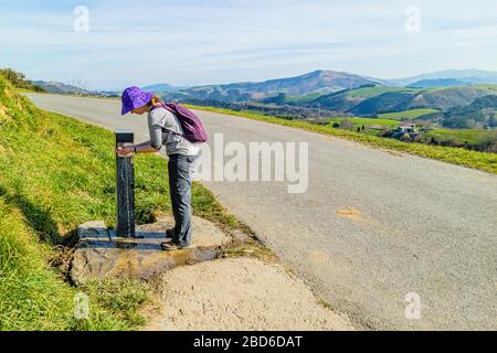 Eine Frau, die sich an einem Brunnen auf dem Camino de Santiago del Norte bei Zumaia im Norden Spaniens abkühlt. Februar 2017. Stockfoto