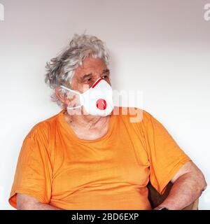 Ein Senior mit einer antiviralen FFP3 N99-Schutzmaske zum Schutz vor Coronavirus. Weißer kaukasischer Mann in einem orangefarbenen T-Shirt an der weißen Wand Stockfoto
