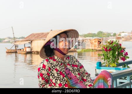 Lächelnde Vietnamesin, die in einem schwimmenden Haus lebt und einen traditionellen konischen Hut am Mekong-Delta, Vietnam, Südostasien trägt Stockfoto