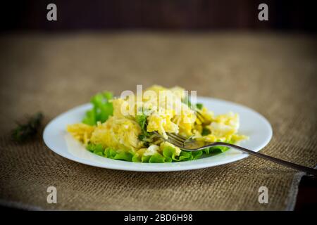 Gebratenes Omelett mit dünnen Vermicelli mit Salatblättern in einem Teller auf einem Holztisch Stockfoto