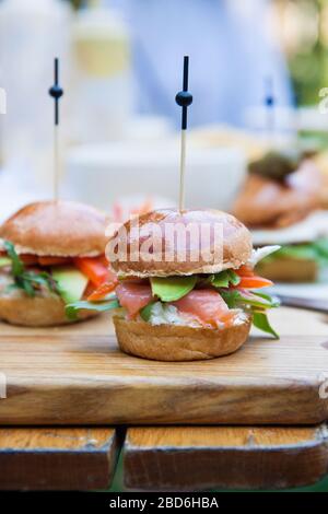 Burger mit Frischkäse, gesalzenem Lachs, Grünkohl, Avocado auf Weizenbun. Rustikaler Hintergrund. Stockfoto