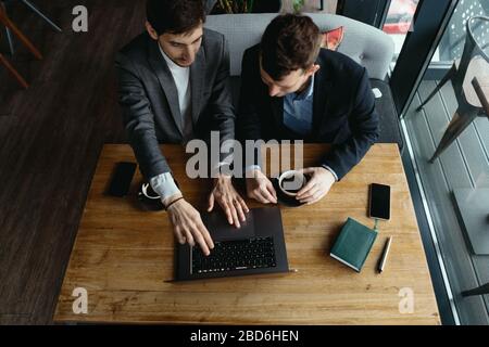 Zwei gutaussehende Geschäftsleute sprechen und zeigen während der Diskussion auf den Bildschirm des Laptops. Geschäft. Technologie. Partnerschaft. Stockfoto