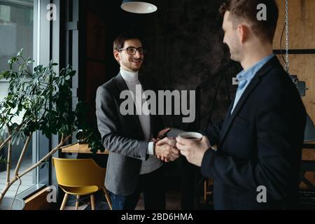 Lächelnde junge Geschäftspartner in Business Casual Wear blicken einander an und schütteln nach Vereinbarung die Hände. Grußkonzept Stockfoto