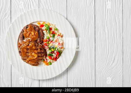 Gegrillte Hamburger mit Zwiebelgravy und Reis, gemischt mit Gemüse auf einem weißen Teller auf einem Holztisch, flacher Lay, freier Platz Stockfoto