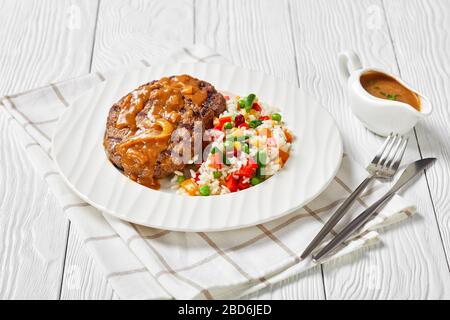 Gehackte Rindersteaks mit Zwiebelgrasgravy und Reis gemischt mit Gemüse auf einem weißen Teller auf einem Holztisch, horizontale Ansicht von oben Stockfoto