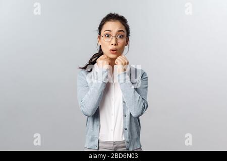 Zaghafte und schüchterne asiatische Mädchen in Brille, brünettes Haar gekämmt, Hände in der Nähe der Brust vergasend halten und mit Mitgefühl oder Sympathie schauen, hören Stockfoto