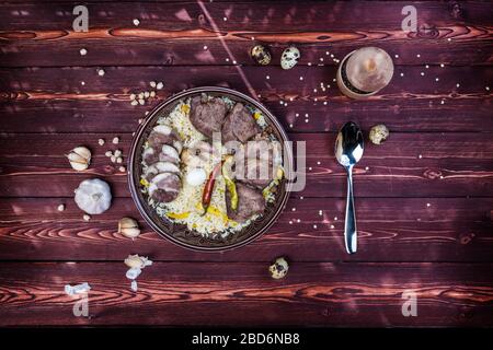 Das Konzept der orientalischen Küche. Nationaler usbekischer Pilaf mit Fleisch. Draufsicht mit Zutaten und einem Löffel, Kopierraum. Stockfoto