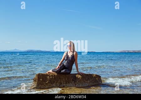 Junge Frau in Sportbekleidung sitzt auf einem Felsbrocken im Meer. Stockfoto