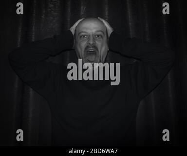 Mann schreit im Dunkeln. Mann mit den Händen auf dem Kopf und schreiend vor Verzweiflung. Stockfoto