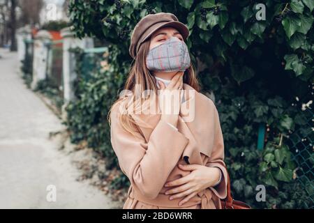 Frau fühlt sich wunde Kehle trägt wiederverwendbare Maske im Freien während Coronavirus Kovid-19 Pandemie. Mädchen fühlt sich krank. Stockfoto