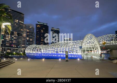 Die Webb Bridge beleuchtete nachts blau und weiß mit hohen Apartments und Bürogebäuden im Hintergrund auf der Southbank Seite des Yarra River. Stockfoto