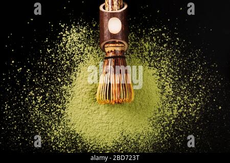 Chasen, spezielle Bambusmatcha-Teewische, die auf pulverförmigen Matcha auf schwarzer Oberfläche liegen. Stockfoto