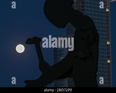 07. April 2020, Hessen, Frankfurt am Main: Der Mond steht als sogenannter Supermond hinter dem berühmten "hämmernden Mann", einem Kunstwerk des US-amerikanischen Künstlers Jonathan Borofsky. Der Mond erreicht in der Nacht vom 7. Auf den 8. April als Vollmond seinen Perigäum, also den Punkt, der dem Erdorbit am nächsten liegt und erscheint daher dem menschlichen Beobachter besonders groß. Foto: Arne Dedert / dpa Stockfoto