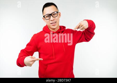 Schöner brunette-asiat in rotem Pullover und Brille für Augenlicht zeigt Finger auf einem Pullover auf weißem Hintergrund Stockfoto
