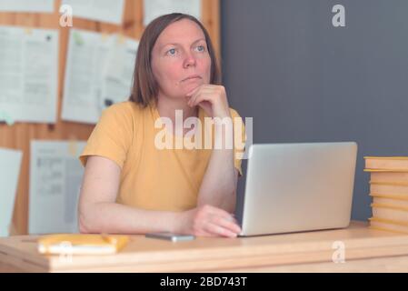 Nachdenkliche freiberufliche Übersetzerin, die im Home Office mit Laptop und Smartphone arbeitet, selektive Fokussierung Stockfoto