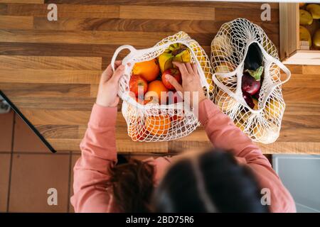 Draufsicht einer Frau, die Obst und Gemüse mit einer wiederverwendbaren Tasche aus biologischer Baumwolle und Netztaschen zum Einkaufen herausnimmt. Kein Abfall, Kunststofffreies Konzept. Stockfoto