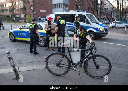 Hamburg, Deutschland. April 2020. Polizisten kontrollieren einen Kapuzenmann, während ein anderer Offizier das Fahrrad des Mannes fotografiert. Die Initiative #LeaveNoOneBeid hatte am Dienstagabend zu einem Protesttreffen mit dem Namen "Umherstreiten für Versammlungsfreiheit" aufgerufen. Nach Angaben der Polizei waren bis zu 200 Menschen auf Fahrrädern im St. Pauli-Gebiet verstreut, die Slogans riefen oder Plakate ausstellten. Die Beamten versuchten wiederholt, die Aktion zu stoppen und übergaben Anklagepunkte. Kredit: Jonas-Walzberg / dpa / Alamy Live News Stockfoto