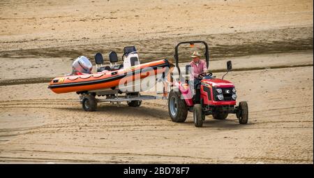 TENBY, PEMBROKESHIRE, WALES - AUGUST 2018: Traktor schleppt bei Ebbe einen Anhänger mit einem aufblasbaren Schnellboot im Hafen in Tenby, West Wales Stockfoto