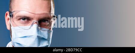 Gesicht von seriösen selbstbewussten Arzt trägt medizinische Schutzmaske und Brille Blick auf Kamera, blaue Kopie Raum Hintergrund. Spezialist für Virologie Stockfoto
