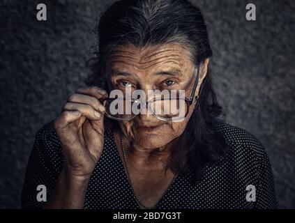 Nahaufnahmen von skeptischer alter Frau, die verdächtig aussehend ist, einige ekelige Missbilligung auf einem isolierten dunkelgrauen Hintergrund. Negative menschliche Emotionen, Stockfoto