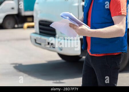 Kurierfahrer in Uniform macht Notizen in Dokument und Lieferung weißer LKW behinde ihn Stockfoto
