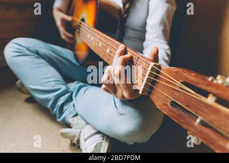 Bleib Zu Hause Bleib Sicher. Junge Frau, die zu Hause sitzt und Gitarre spielt, Hände nah dran. Teenager-Mädchen lernen, Lied zu spielen und Musik zu schreiben. Hobby Lifestyle Relax Instrument Freizeit Bildungskonzept Stockfoto