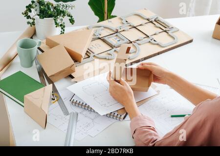 Box Maker arbeitet hinter einem Tisch, falten, Formen einer Schachtel, Werkzeuge verstreut Stockfoto