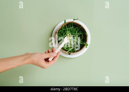 Frau, die Erbsensprosse aus umweltfreundlichen Gerichten isst. Nur Hand. Draufsicht Stockfoto