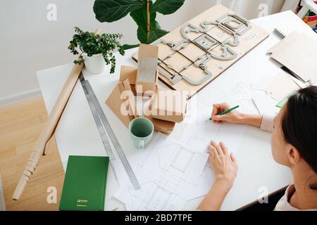 Box Maker arbeitet hinter einem Tisch, zeichnet Skematiken, verteilt auf Werkzeuge Stockfoto